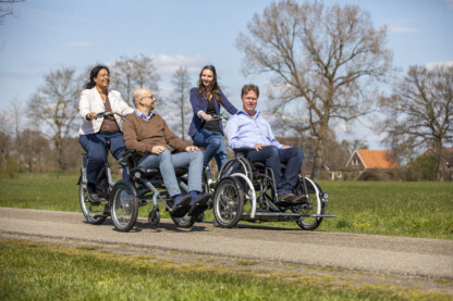 Quatre personnes découvrent la Normandie en vélo adapté sur une route ensoleillée, entourées de verdure.