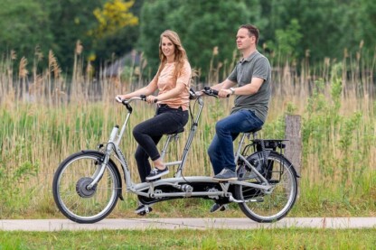 Deux personnes souriantes pédalent ensemble sur un vélo adapté, entourées de verdure en Normandie.