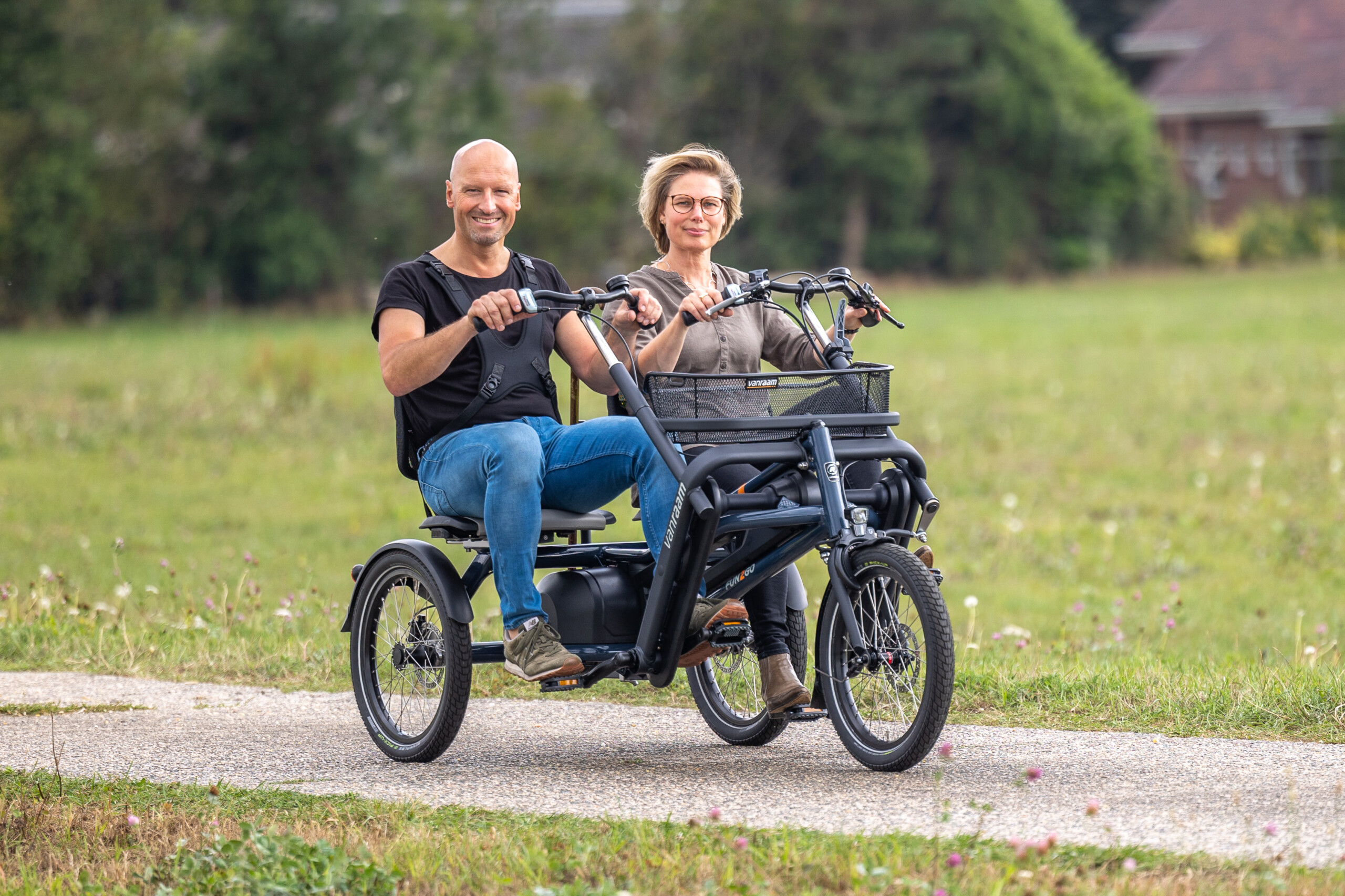 Deux personnes souriantes sur un vélo à trois roues, circulant sur un chemin en pleine nature.