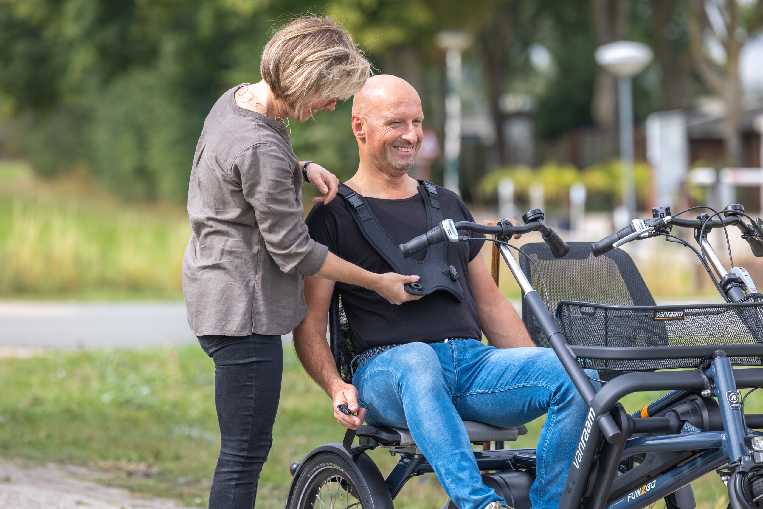 Personne aidant un homme à s'installer sur un vélo adapté, en pleine nature.