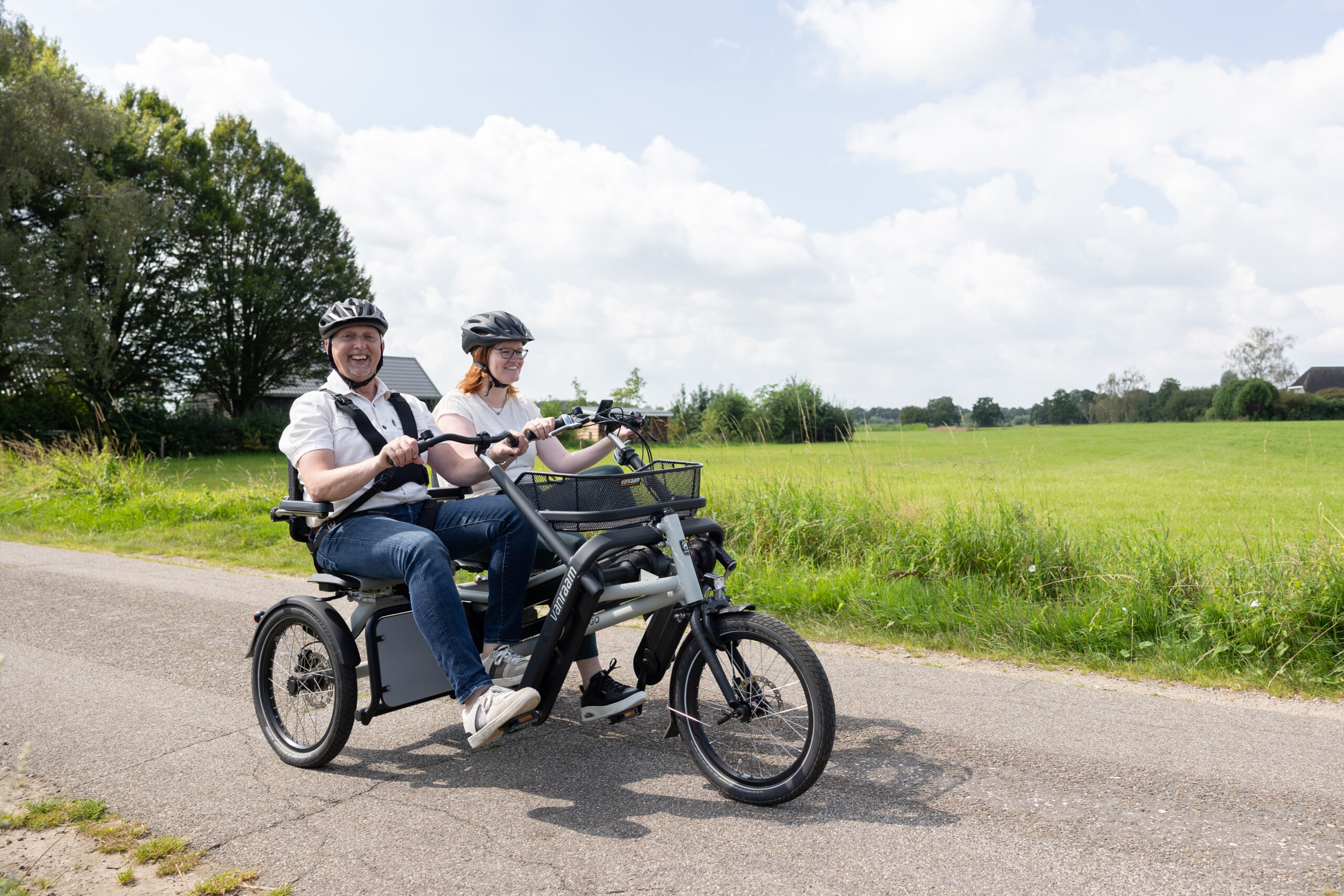 Deux personnes souriantes font une balade à vélo dans la campagne normande sur un vélo adapté.