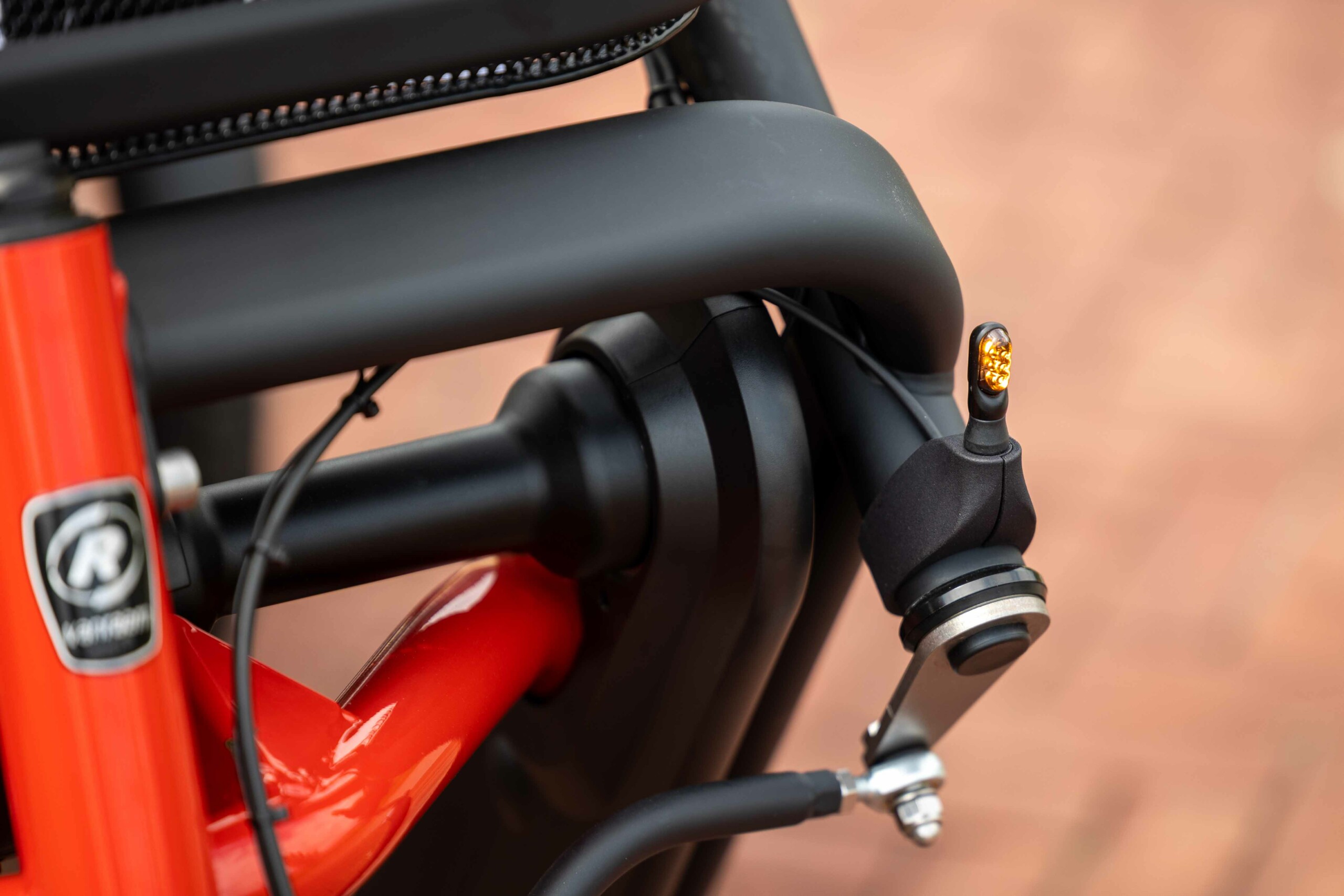 Détail d'un cadre de vélo rouge et noir avec un clignotant en activé, idéal pour les balades en Normandie.