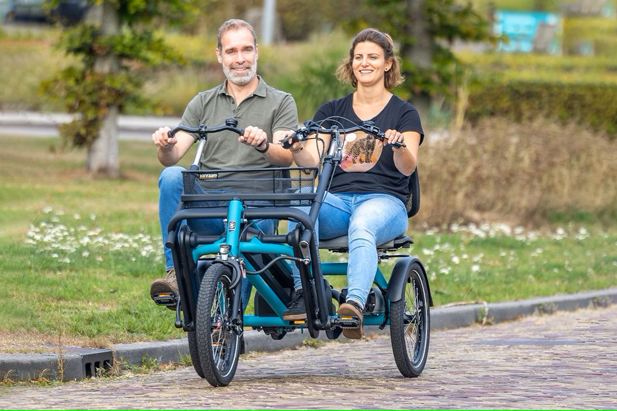 Deux personnes souriantes roulent sur un vélo à trois roues dans un parc, idéales pour des balades en Normandie.