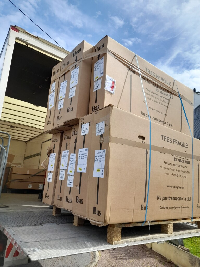 Cartons de vélos en attente de livraison, étiquetés "très fragile", dans un camion.